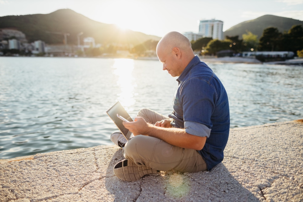 Mann sitzt mit Laptop am Ufer Wireless Life Rocks